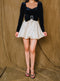 Long sleeve, black dress has ribbon belt and beige, satin bow swing skirt.